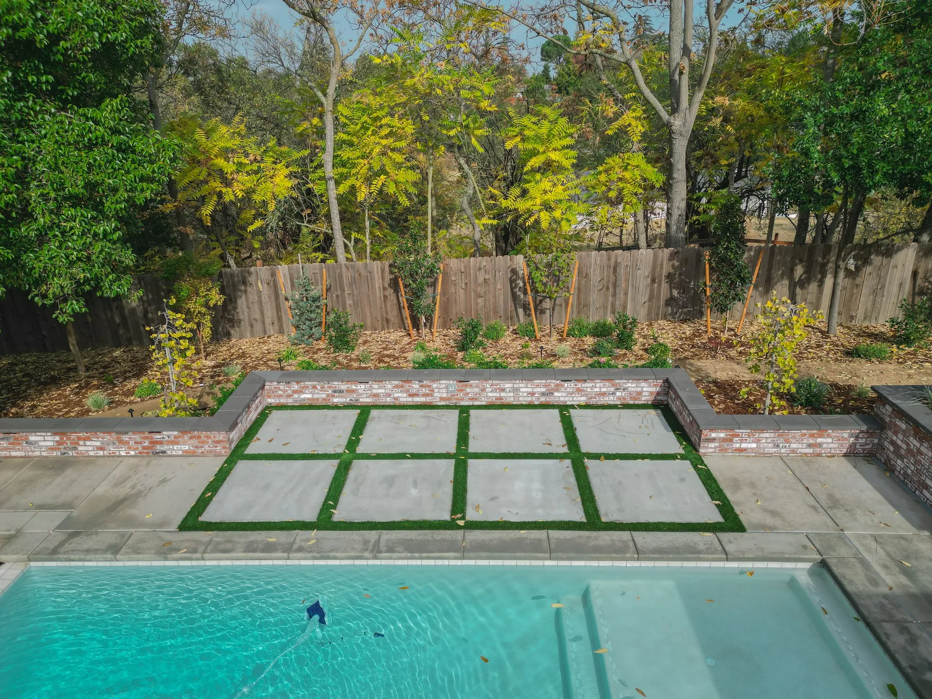 Paver patio with turf inlay, brick retaining wall, and pool in a Sacramento backyard