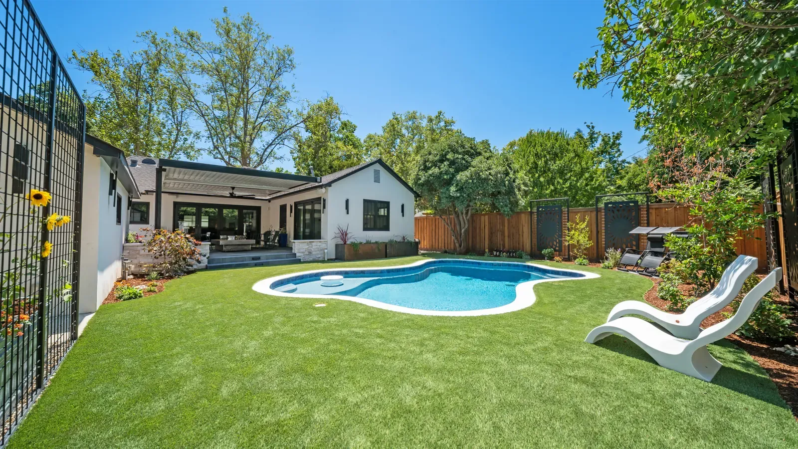 Finished backyard with a pool, turf lawn, and plantings by Stuteville Landscaping