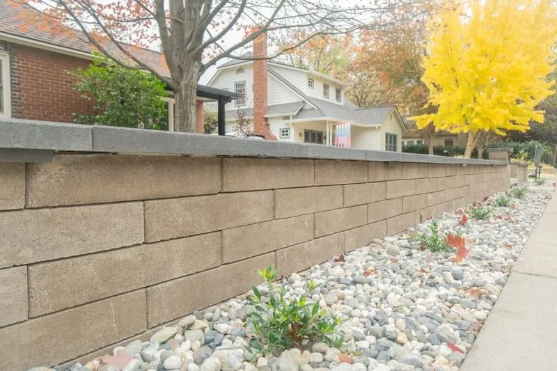 Block retaining wall with cap stones and river rock planting bed along a Sacramento sidewalk