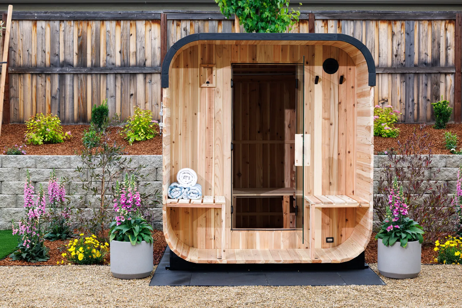 Cedar barrel sauna in front of a block retaining wall with flowering plantings