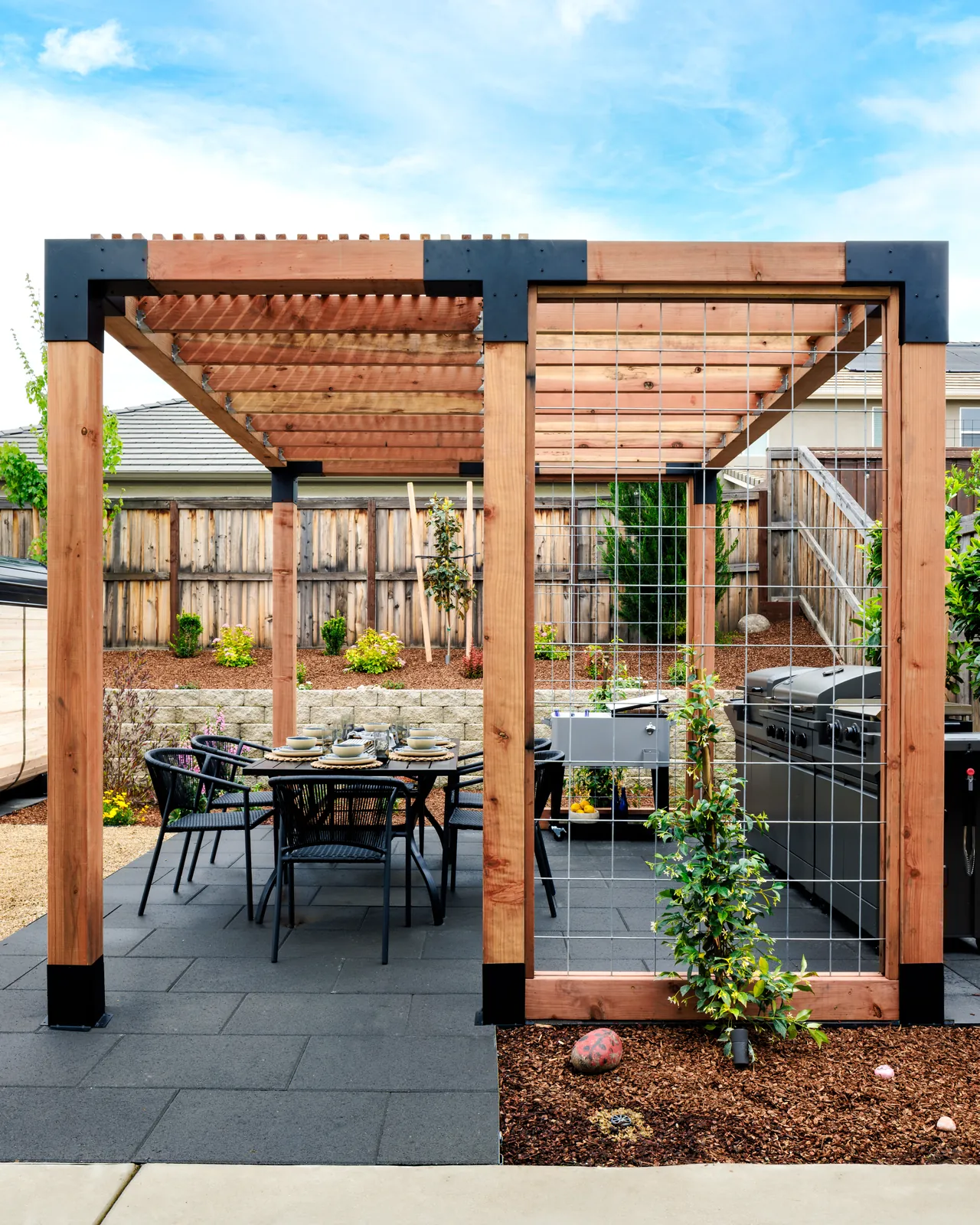 Cedar and steel pergola over an outdoor dining table and kitchen
