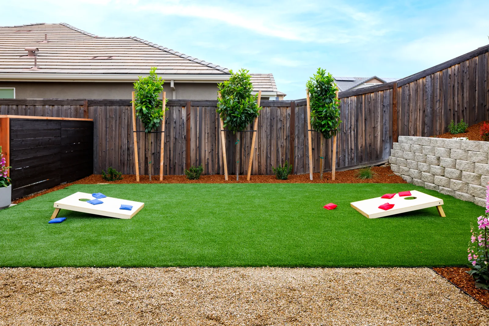 Synthetic turf games lawn with cornhole boards and new trees along the fence