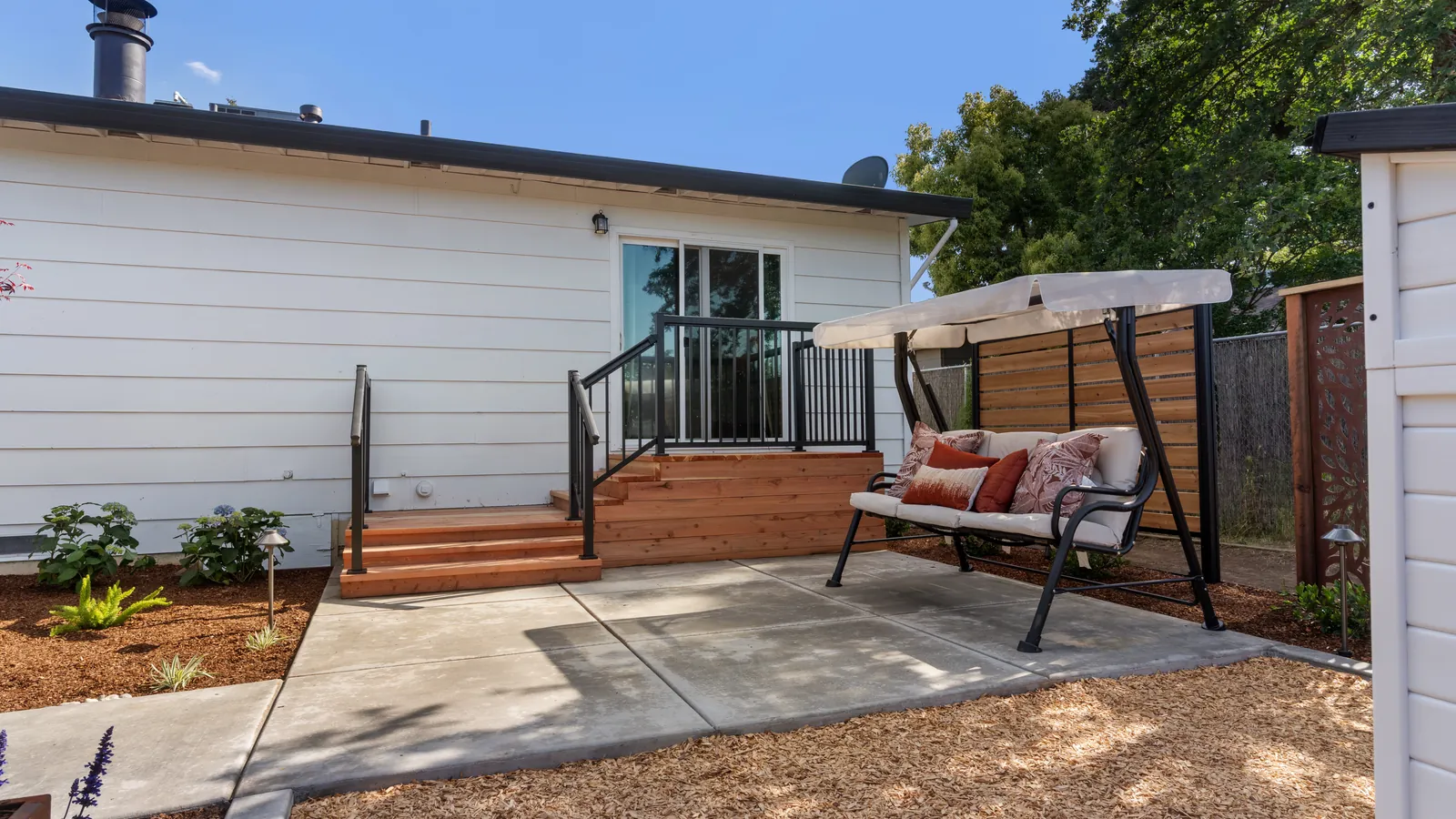 After: redwood steps with black metal railings down to the patio and a covered swing