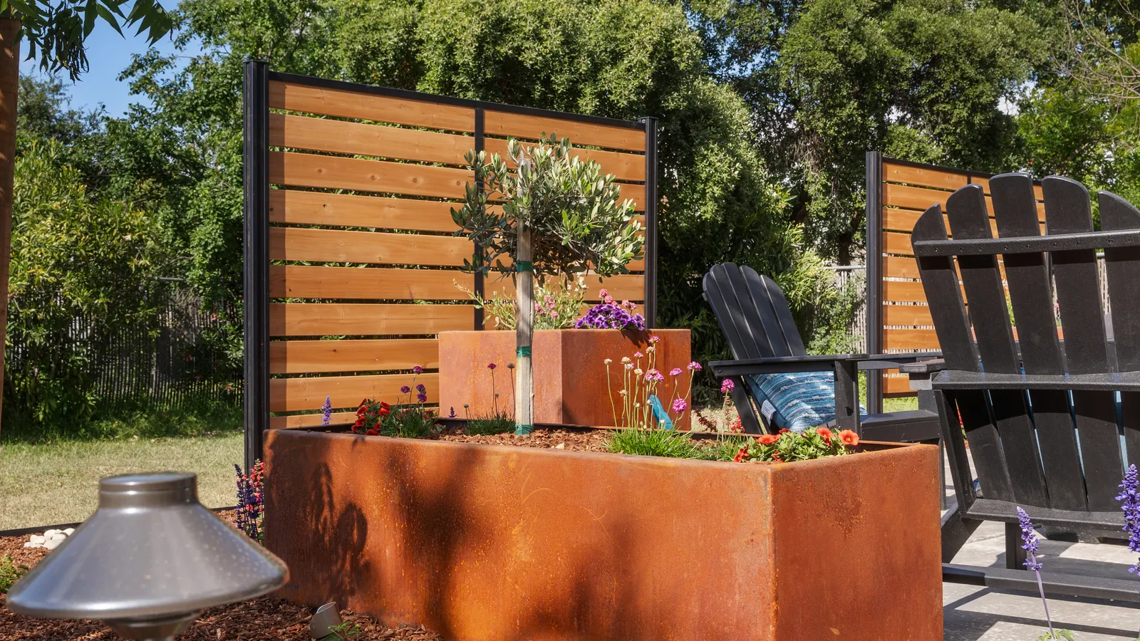 Corten steel planter with a young tree beside Adirondack seating and a cedar screen
