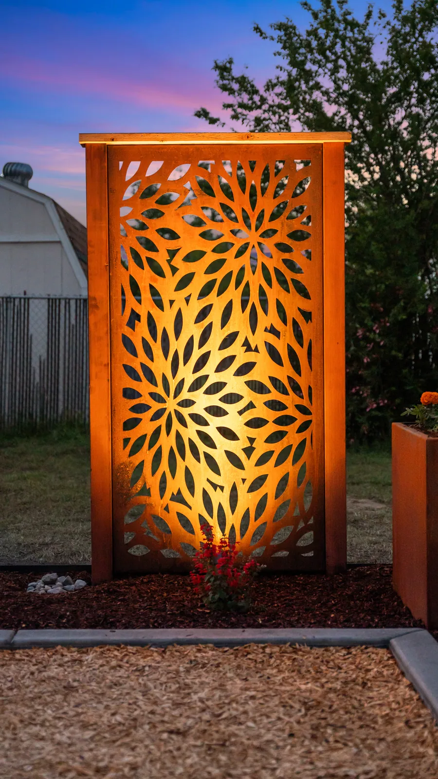 Laser-cut corten steel privacy screen lit from below at dusk