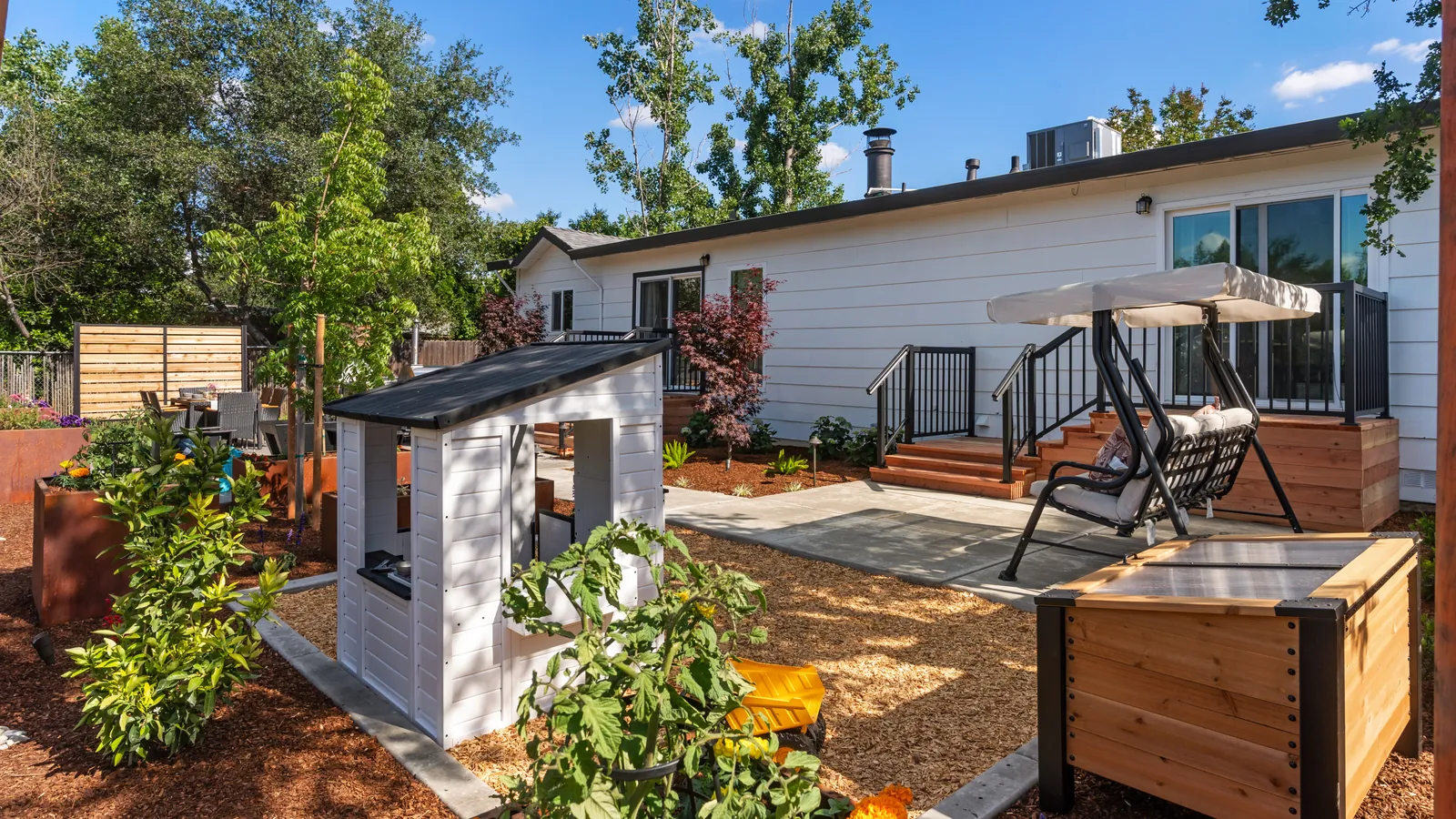 White playhouse and covered swing on pea gravel beside the house