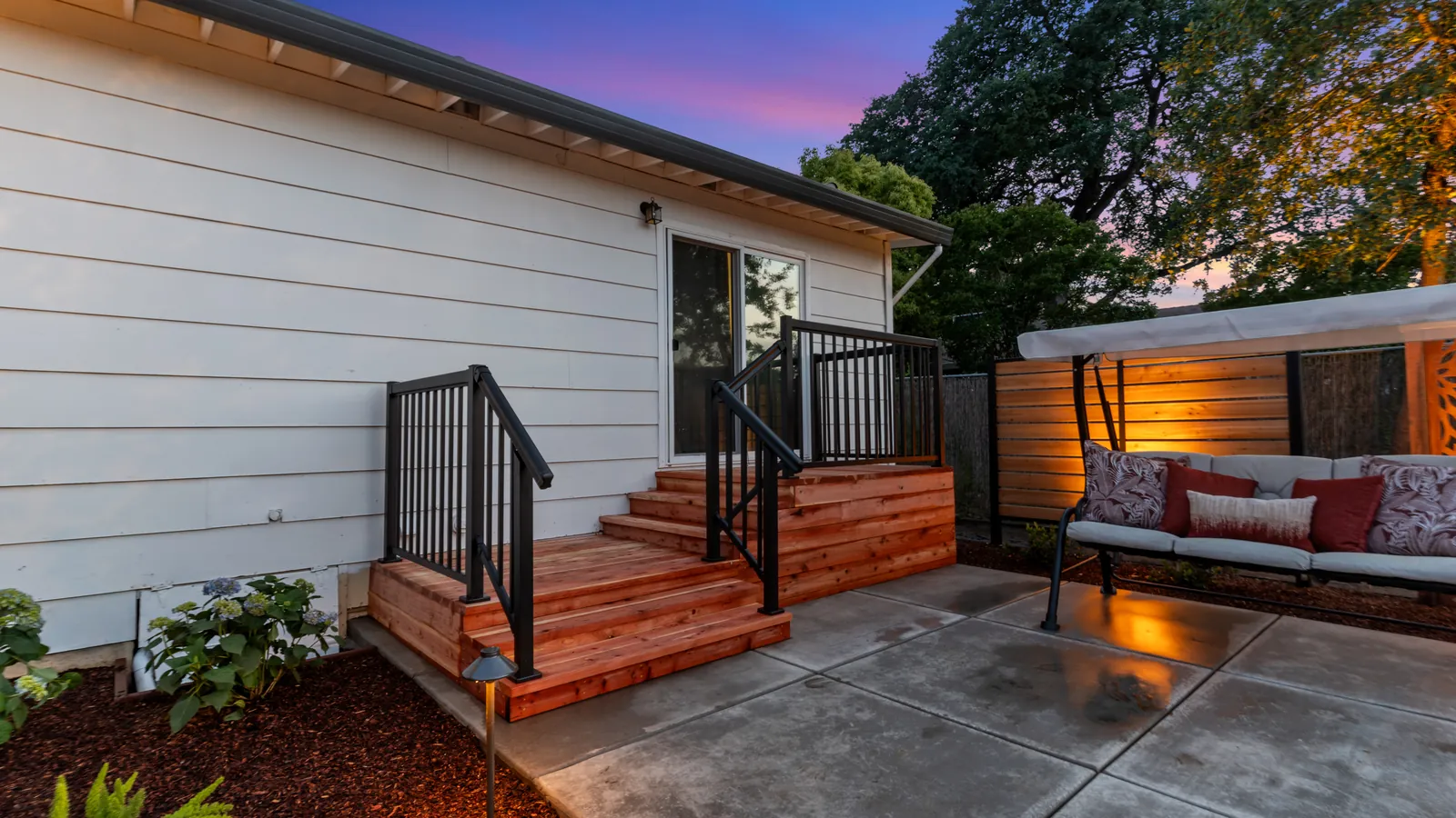 Redwood steps with black metal railings leading to a lit covered swing