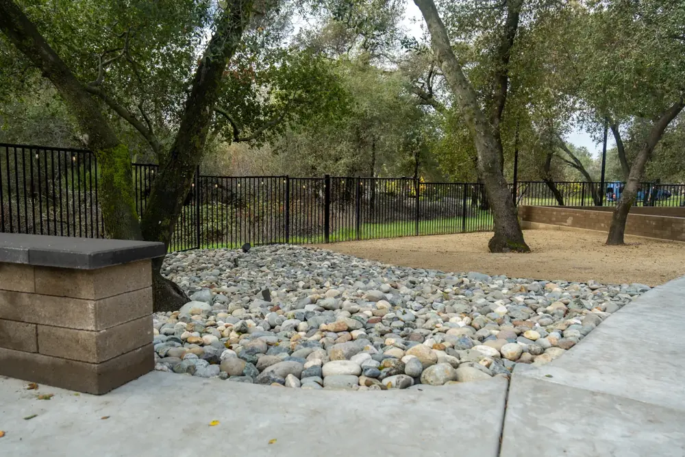 River rock drainage swale beside a block wall and concrete walkway