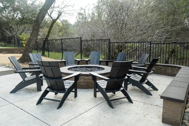 Round fire pit surrounded by Adirondack chairs on a concrete patio