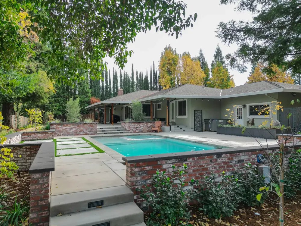 Pool deck with concrete pavers set in a turf grid and a brick retaining wall by Stuteville Landscaping