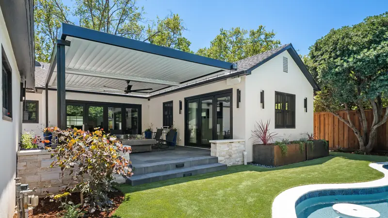 Louvered pergola over a patio beside a pool and turf lawn